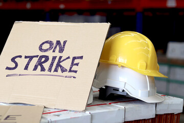 On strike banner placard with two white and yellow worker helmets at cargo logistic warehouse....