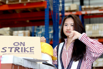 Angry unhappy young Asian woman wearing safety vest, holding helmet and giving thumb down standing...
