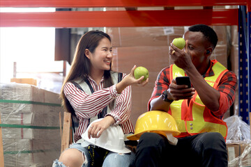 Asian woman staff wearing safety vest, giving apple to colleague African worker during eating lunch...