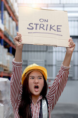Angry unhappy Asian woman worker wearing safety vest and helmet, holding and raising sign on strike...