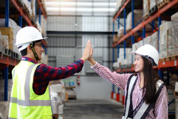 Young Asian woman and her senior supervisor with safety vest and helmet making high five hand touch...