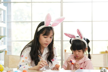 mother teaching happy little kid soon to dye and decorate eggs with paints for Easter holidays sitting together at living room .Easter Family traditions