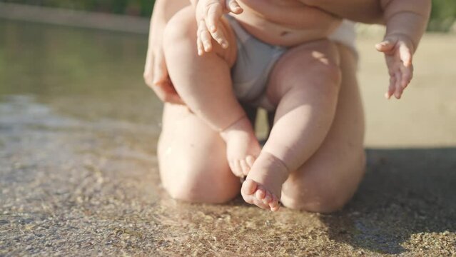 Closeup of baby feet caressed by waves. Beautiful mother playing with little baby boy on beach together. Soft touch, love, protection of mom and child relationship. Mom and cute baby resting by sea.