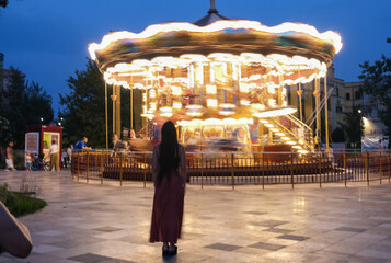 Woman in front of a Carousel circus spinning with light trails. Long exposure.