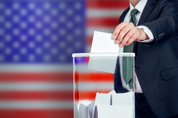 A voter casts a ballot into a ballot box on election day, USA flag