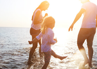 Happy young family having fun running on beach at sunset - obrazy, fototapety, plakaty
