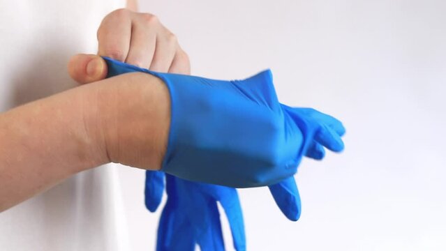 Nitrile gloves for cleaning, disposable. Women's hands put on blue gloves on a light background, cleaning, close-up. Gloves to protect hands from moisture and detergents