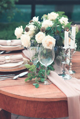 Candles and vase with white roses placed on round table near wineglasses