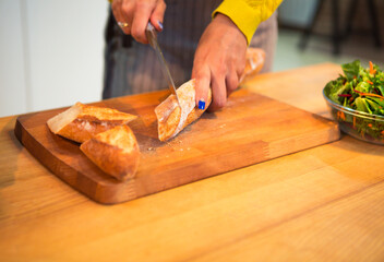 Cropped shot of woman cutting baguette bread on the tabletop