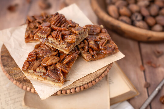 Close-up of Homemade Pecan Bars on Pedestal with Bowl of Pecans in Background