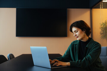 Young business woman working on laptop. Flexible office for startups. Creative female looking into...