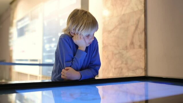A child of primary school age visiting a science museum. The boy is exploring information about the exhibition exhibits on an interactive touch screen display