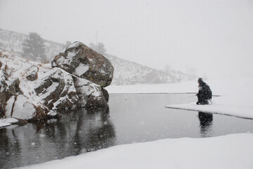 An ice fisherman fishing on the edge of the ice during a snow storm. 