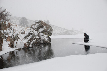 An ice fisherman fishing on the edge of the ice during a snow storm. 