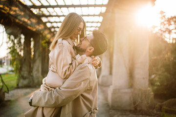 Close-up shot of a beautiful couple posing in a park garden on a spring sunny day. A man holds a woman in his arms. Family, love and happiness concept. - obrazy, fototapety, plakaty