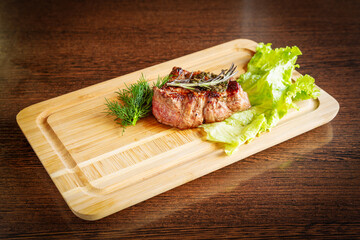 Grilled beef steak with lettuce on a wooden board.