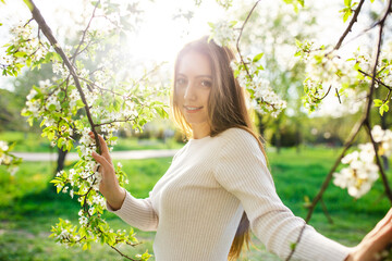A stunning woman with long hair posing in a spring garden during sunset on a beautiful sunny day. The concept of femininity, happiness and love. - obrazy, fototapety, plakaty