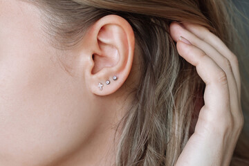 Ear piercing. Cropped shot of a young woman wearing three stud earrings on the earlobe. Jewelry...