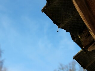 a drop of water drips from an old roof as the snow melts