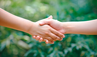 Handshake on a green background. Blurred nature background. Two hands reach out to each other. The concept of friendship and mutual assistance. Support. Help.