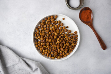 Roasted chickpeas with smoked paprika and salt on a light background in a white plate. View from above. Healthy seasoned chickpeas with various spices