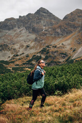 Stylish hiker woman with sunglasses and backpack walking in Hight Tatras mountains, Poland. Magestic big rock on background