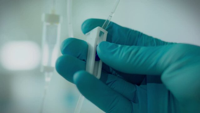 Operating room. The procedure in protective gloves slowly sets up iv drip in the hospital. Camera in motion young professional installs iv drip using modern technology, transfusion