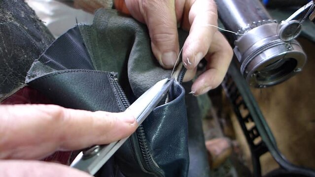  Repair of old shoes at a craftsman specialized in repairing all types of shoes. Cutting the excess thread with scissors after sewing a zipper on an old manual sewing machine