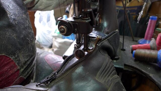 Repair of old shoes at a craftsman specialized in repairing all types of shoes. Close-up of repairing old leather shoes, quilting the zipper on an old sewing machine