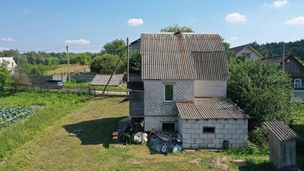 Rough two-story small country house made of bricks and blocks with slate gable roof in gray. A house without architectural design in Europe. A hermit's house with a garage. House of introvert, maniac.