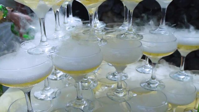 Tower of drinks, a slide of champagne with dry ice and smoke at a party. Glasses of champagne stand side by side, the waiter fills the glasses with wine, buffet at a social event.