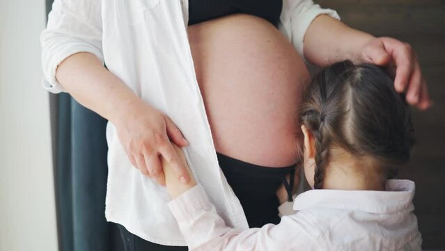 The affection and tenderness of a pregnant mother and daughter. A girl strokes the belly of a pregnant mother with her unborn brother. A sweet girl worries and takes care of her mother.