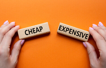 Cheap or Expensive symbol. Concept word Cheap or Expensive on wooden blocks. Businessman hand. Beautiful orange background. Business concept. Copy space