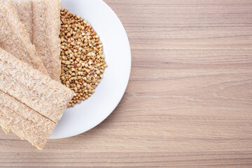 Buckwheat crisp bread and buckwheat on plate on wooden background, gluten free. Dietary cookies