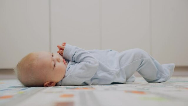 Child development, turning over before crawling. The baby boy is lying on his back and is nervous because he cannot roll over onto his stomach. The baby learns to perform flips.