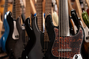Closeup of row of different colorful bass guitars on the display for sale hanging in a music shop 