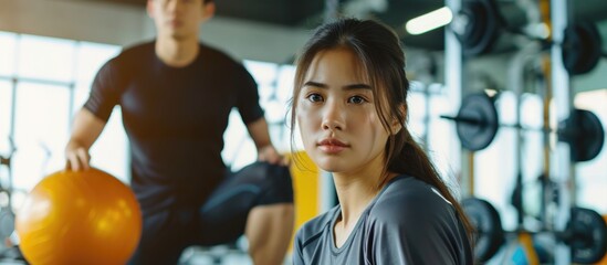 Asian woman doing squat legs near personal trainer in gym, leading healthy lifestyle with cardio training for weight loss.