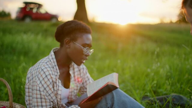 Multiethnic group of young People Study Holy Bible outdoors in Park at picnic on summer Sunset. Diverse Christian Students read Scripture. Students with books studying outdoors. 4K zoom out shot