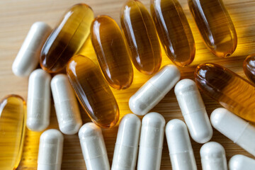 closeup of white, yellow medicine capsules on a wooden table.