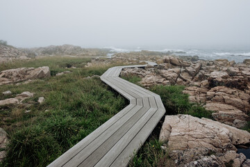 M&oslash;llen&aelig;sstien in Allinge, Bornholm. Walking on a wooden path through granite landscape near the sea on a misty day.