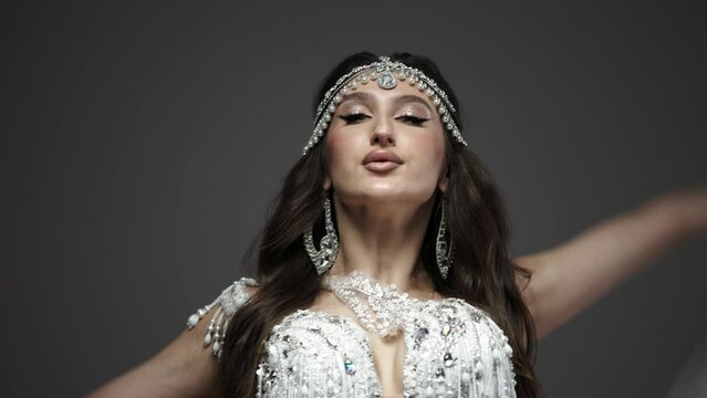 Belly and body of a woman dancing oriental dance in the studio, making beautiful body movements, she is dressed in a chic white suit on a dark background of the studio. The concept of beautiful images