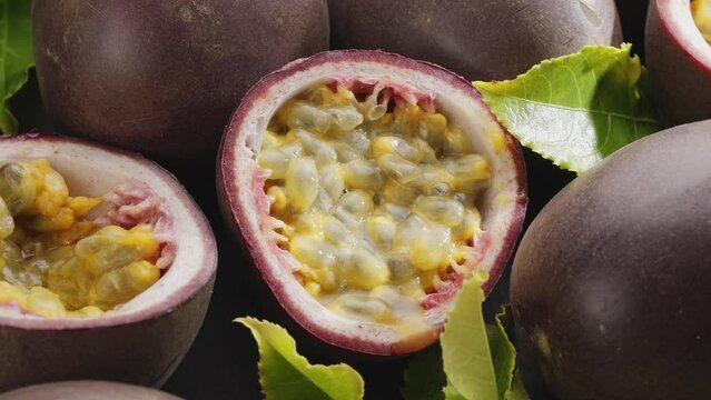 Ripe passion fruits with passion fruit seeds and passionfruit leaves slowly move in the frame on a gray stone table.