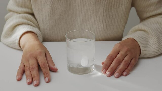 Woman sitting in front of glass of water with effervescent tablet, waiting for its total dissolving.