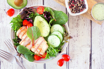 Healthy homemade salad bowl with avocado and chicken. Above view table scene on a white wood background.