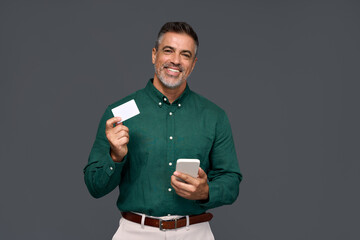 Happy middle aged business man, smiling mature businessman holding mobile phone and credit debit card mockup using banking finance app making online purchase on smartphone isolated on gray background. - obrazy, fototapety, plakaty