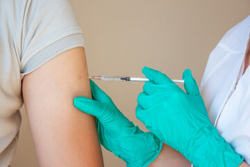 A doctor in green gloves gives a young man an intramuscular injection for the virus and flu....