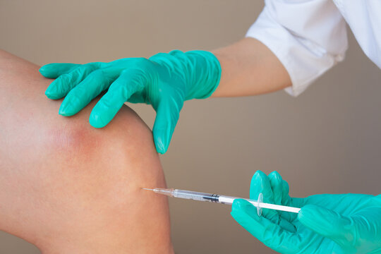 A doctor in green gloves gives a young man an intra-articular injection of hyaluronic acid against osteoarthritis in the knee joint. Preventing the destruction of the knee joint.