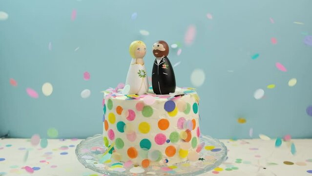 Bride and groom wedding cake toppers on wedding cake with colorful falling confetti slow-motion