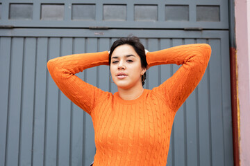 Confident woman standing with hands behind head against gray wall