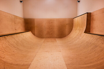 An indoor skateboard sports ramp / halfpipe lit by spotlights with no people, wooden texture and...